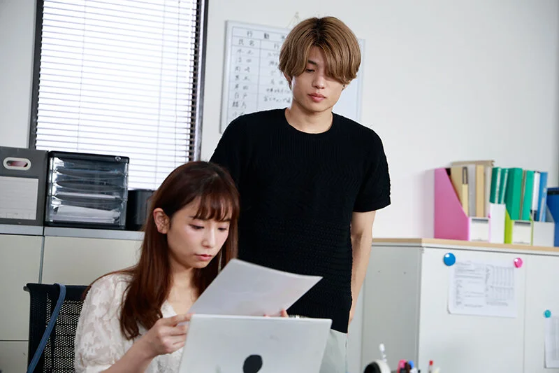 書類を手にする彼女を見つめる保志健斗。抑えきれない想いが視線ににじむオフィスシーン