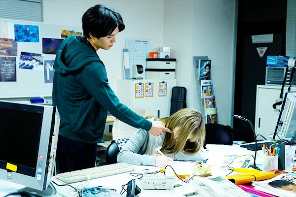 机に突っ伏す彼女を気づかう彼。さりげない優しさが、胸にじんわり残る。